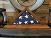 Triangular wooden flag case with visible miter joints holding folded American flag stars section.