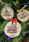 Three personalized wood slice Christmas ornaments with burned lettering and decorative bows hanging on a pine tree branch