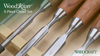 Close-up of six WoodRiver bench chisels with wooden handles and polished steel blades arranged on a wooden surface.