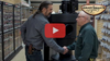 Two men shaking hands next to a large dust collector in a woodworking store aisle