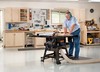 Woodworker wearing hearing protection using a table saw to cut wood in a well-organized workshop.