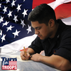 Woodworker handcrafting a wooden pen with American flag backdrop for troop support campaign