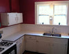 L-shaped kitchen countertop with white cabinets, double sink, and gas stove in workshop setting