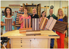 Group of six woodworkers in workshop holding various striped hardwood cutting boards made from mixed wood species
