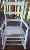 Worn white wooden rocking chair with slatted seat and ladder back on porch floorboards