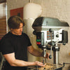 Woodworker adjusting drill press with wood shavings on the table in workshop