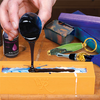 Pouring black resin into a yellow silicone mold with resin tools on a wooden workbench