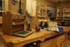 Woodworking bench with wooden tool chest, carved wood sculptures, and hand tools in a workshop setting