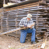 Man measuring moisture content of air-dried lumber stacked with spacers outdoors