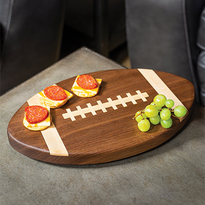Oval walnut cutting board shaped and inlaid to resemble a football with light wood stripes and laces, holding crackers with