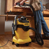Person using a handheld power sander on a wood workbench with a yellow Kärcher shop vacuum nearby on a hardwood floor