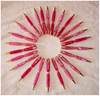 Circle of pink woodturned pens arranged on a light fabric surface in a workshop setting