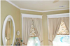 Room corner showing installed white crown molding and window trim with beige curtains and valances